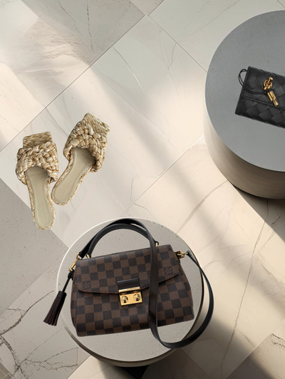 Brown checkered handbag with gold lock on a light gray surface, surrounded by shoes and a small black bag.